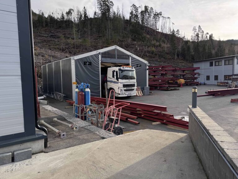 Stålrammer og truck ved bygg- og byggeplass i skogsområde.